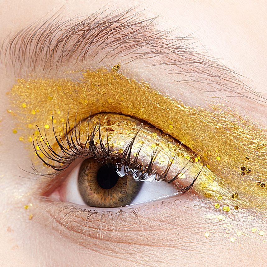 Closeup macro shot of  human female eye. Woman with unusual glitter glitzy vogue face beauty makeup. Girl with perfect skin and yellow smoky eyes eye shadows