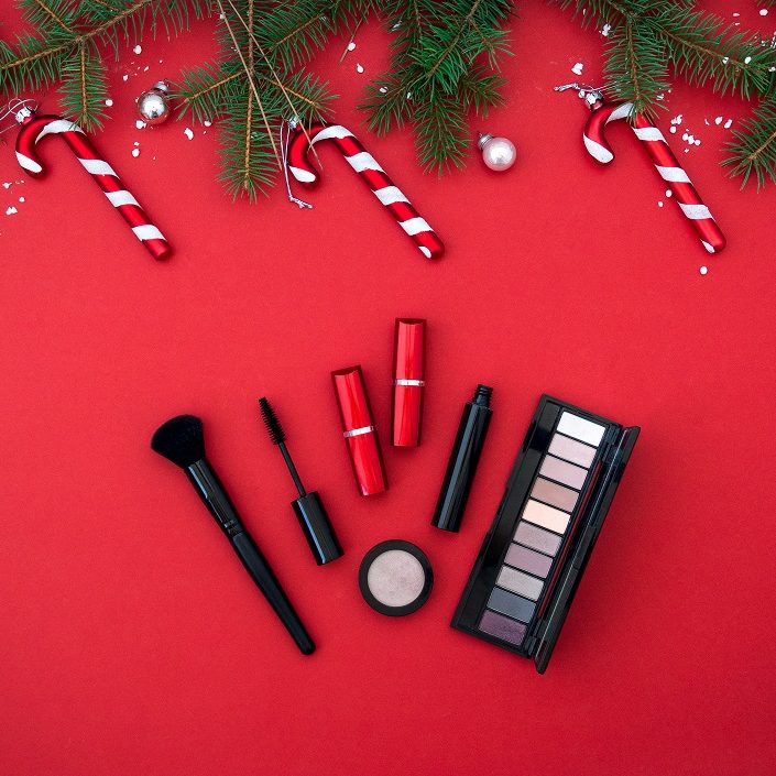 Flat lay composition with makeup cosmetic products and Christmas decor on red background. Top view. Beauty banner for sale.