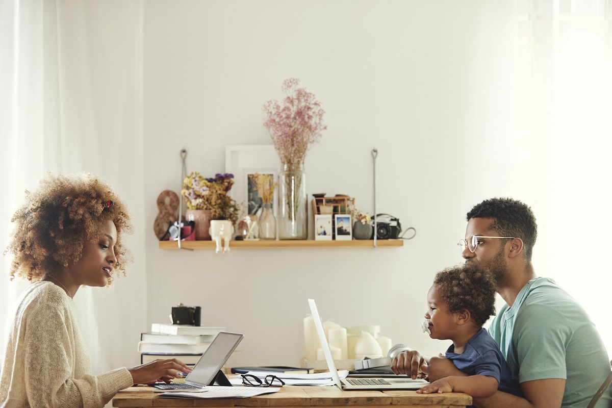 Young woman using digital tablet for working from home. Man using laptop with son at table. They are sitting in kitchen.