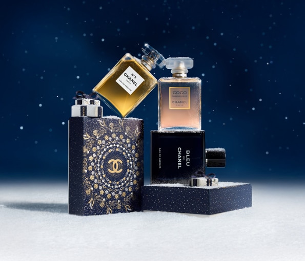 Chanel fragranze iconiche con flaconi N°5, Coco Mademoiselle e Bleu de Chanel su sfondo blu con dettagli neve.
