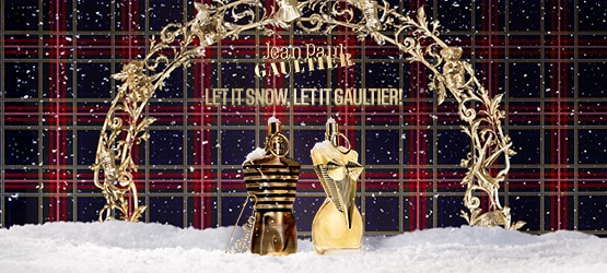 Flaconi di profumo Jean Paul Gaultier dorati su sfondo scozzese con neve e arco decorativo, testo Let It Snow, Let It Gaultier.