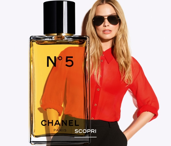 Flacone del profumo Chanel N°5 in primo piano con liquido ambrato, sovrapposto a una figura in camicia rossa su sfondo chiaro.