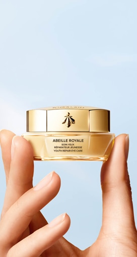 Crema contorno occhi Guerlain Abeille Royale tenuta tra le dita, mostrata su sfondo chiaro con packaging dorato.