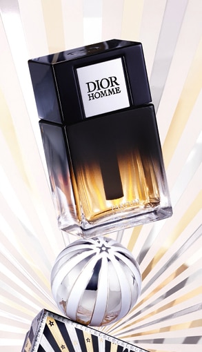 MIT2025-WK51-Dior-CP-Grid-Banner-2.jpg Flacone Dior Homme Parfum sfumato nero e ambra con decorazione argentata su sfondo a raggi luminosi.