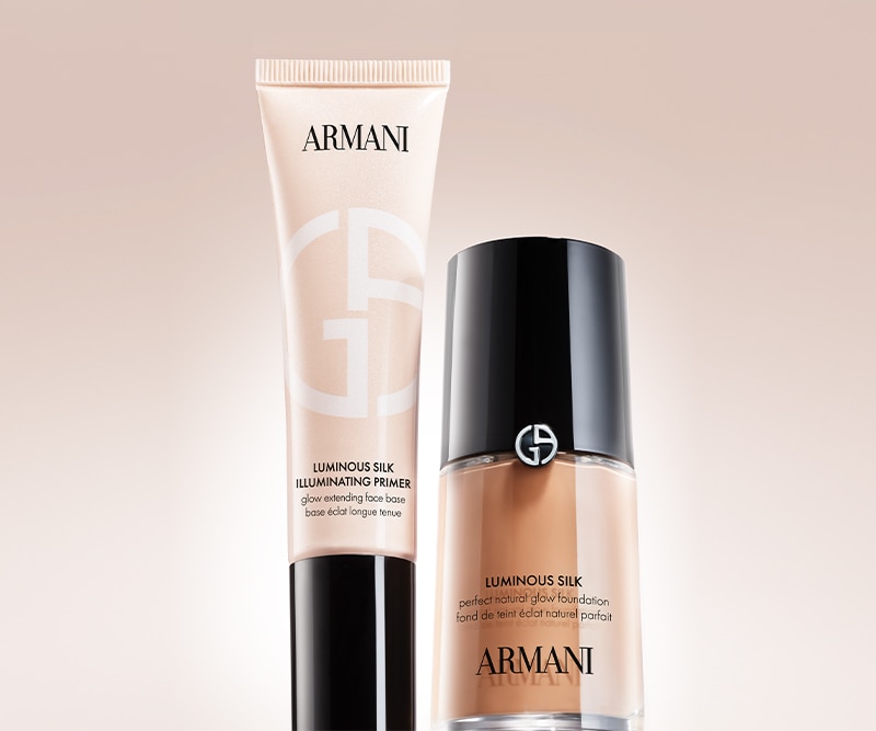Primer illuminante Armani Luminous Silk e fondotinta Luminous Silk esposti su sfondo beige, con pack elegante nei toni nude e nero che evidenziano il finish naturale e luminoso della linea make‑up Armani.