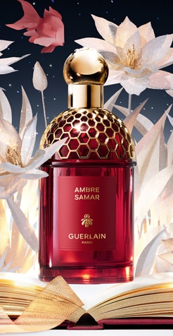 Flacone Guerlain Ambre Samar rosso e oro su sfondo floreale bianco con libro aperto.
