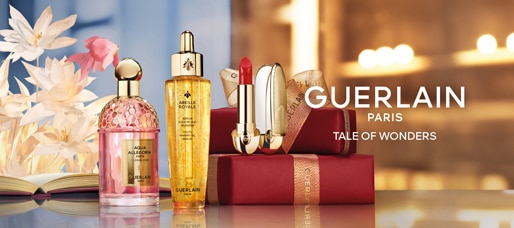 Gift set Guerlain con flaconi dorati e rosa, rossetto rosso e confezioni regalo rosse, testo Tale of Wonders.