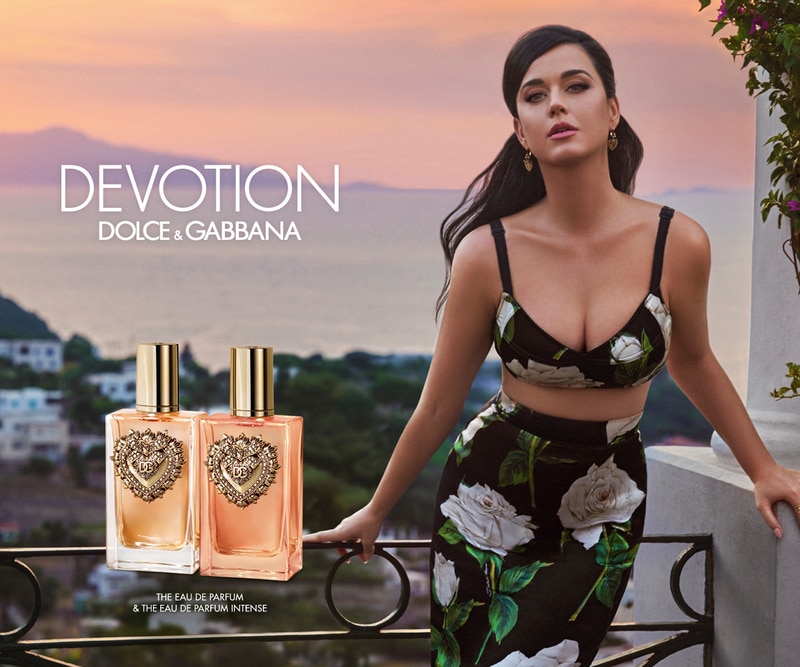 Profumi Devotion Dolce &amp; Gabbana con flaconi eleganti e cuore dorato, vista panoramica al tramonto sul mare, testo Devotion Dolce &amp; Gabbana.