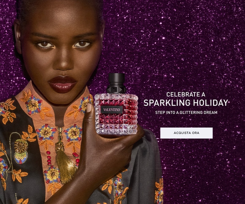 Bottiglia di profumo Valentino su sfondo viola glitterato con testo promozionale “Celebrate a Sparkling Holiday”.