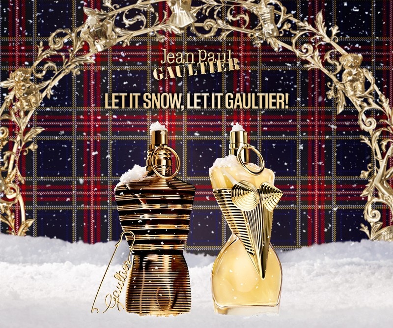 MIT2025-WK51-JPG-HP-Banner.jpg Flaconi dorati su sfondo scozzese con neve, testo Let It Snow, Let It Gaultier.