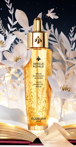 Guerlain Abeille Royale siero viso con perle dorate e sfondo floreale raffinato.